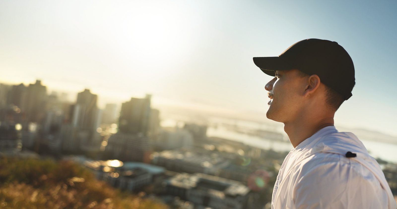 A person in a ball cap looks out over a city at sunrise